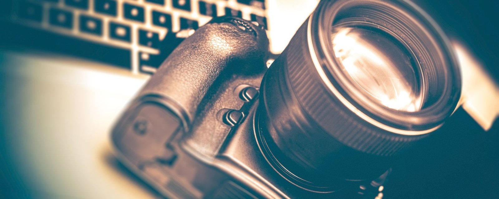 A camera and lens lying on a desk beside a keyboard, in teal tones