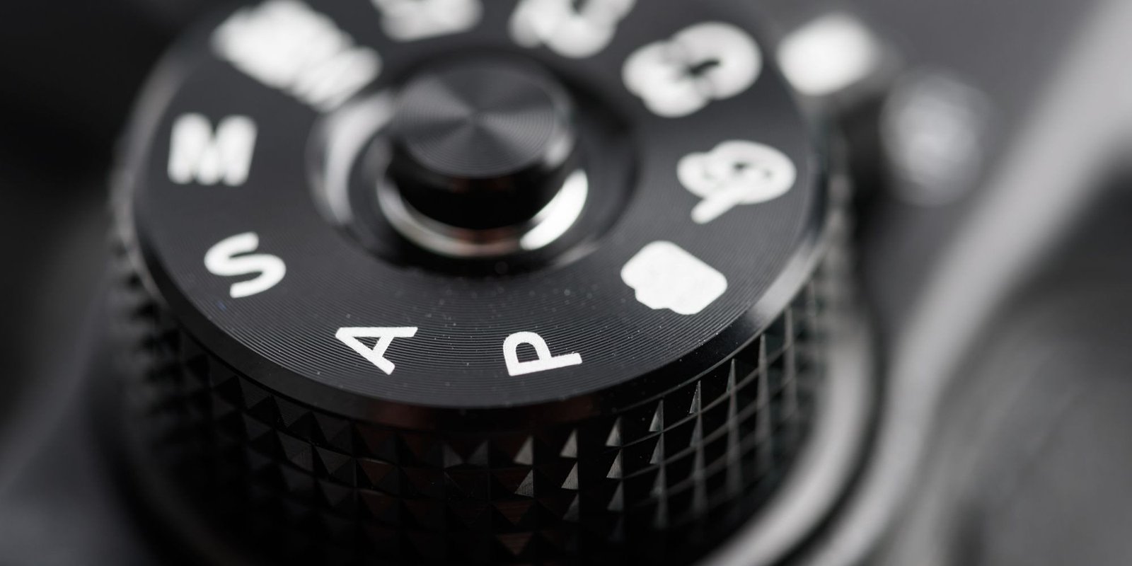 Black and white close up of a camera mode dial, auto and manual settings