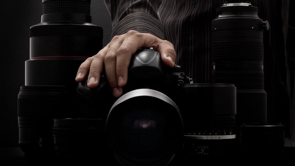 A hand resting on a camera among large lenses on a dark studio table