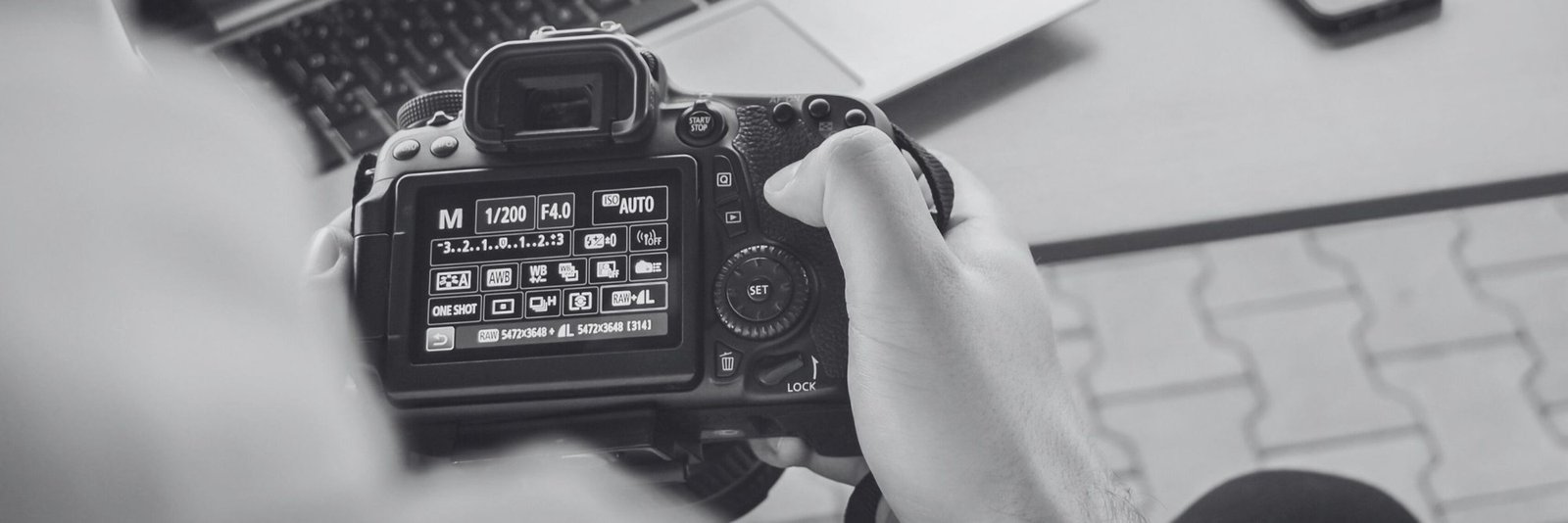Hands holding a camera with its settings screen lit, learning photography online