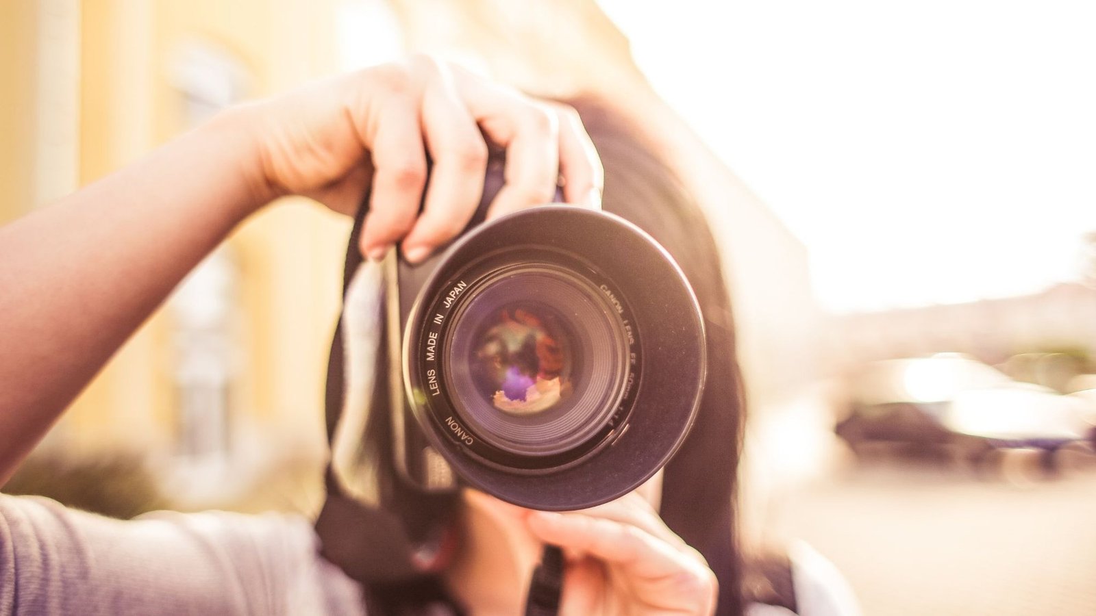 A woman looking through her camera, the lens pointing straight at the viewer
